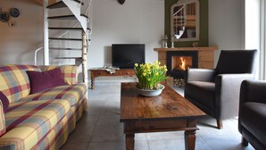 Een gezellige woonkamer met een geruite bank, een houten salontafel met een bloevas, een open haard en een televisie.
