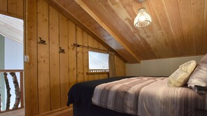 Een kamer met houten lambrisering, een bed, een raam met zonwering en een plafondlamp.