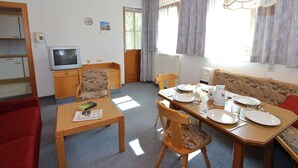 A cozy room with a wooden ceiling, a dining table set with plates, glasses, and cutlery, and a television on a wooden cabinet.