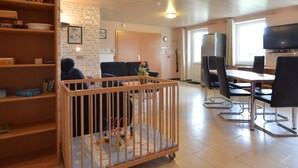 Una habitación con una cuna, una mesa de comedor con sillas, un televisor y una estantería.