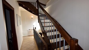 Uma escadaria com guarda-corpos de madeira e piso revestido de azulejos bege, levando a um andar superior.