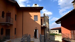 Uma passagem estreita ladeada por edifícios, com varandas, uma torre de pedra e um caminho de azulejos.