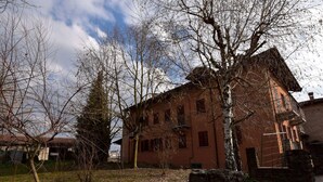 Um edifício rústico com fachada de tijolos, rodeado por árvores sem folhas e uma área gramada.