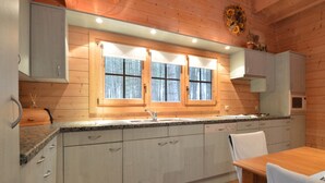 Une cuisine avec des murs en bois, un plan de travail en granit, un évier, des placards et une table à manger avec des chaises.