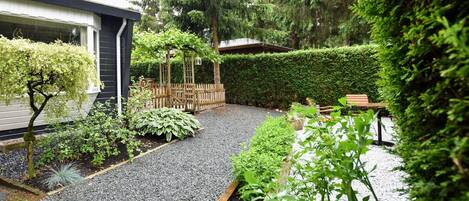 A garden with a gravel path, wooden raised beds, and a wooden pergola.