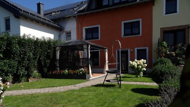 Ein Garten mit einem Pavillon, einer Schaukel und einem Weg zu einem Gebäude mit zahlreichen Fenstern.