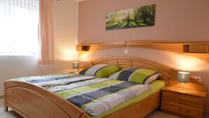Ein Schlafzimmer mit einem hölzernen Bett, einem Nachttisch, einer Nachttischlampe, einem Fenster mit Vorhängen und einem Gemälde an der Wand.