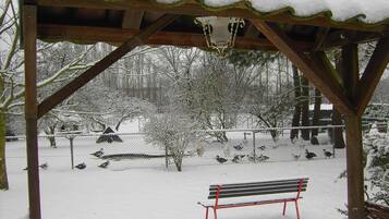 A wooden gazebo with a bench in the center, surrounded by a snow-covered area with trees and a fence.