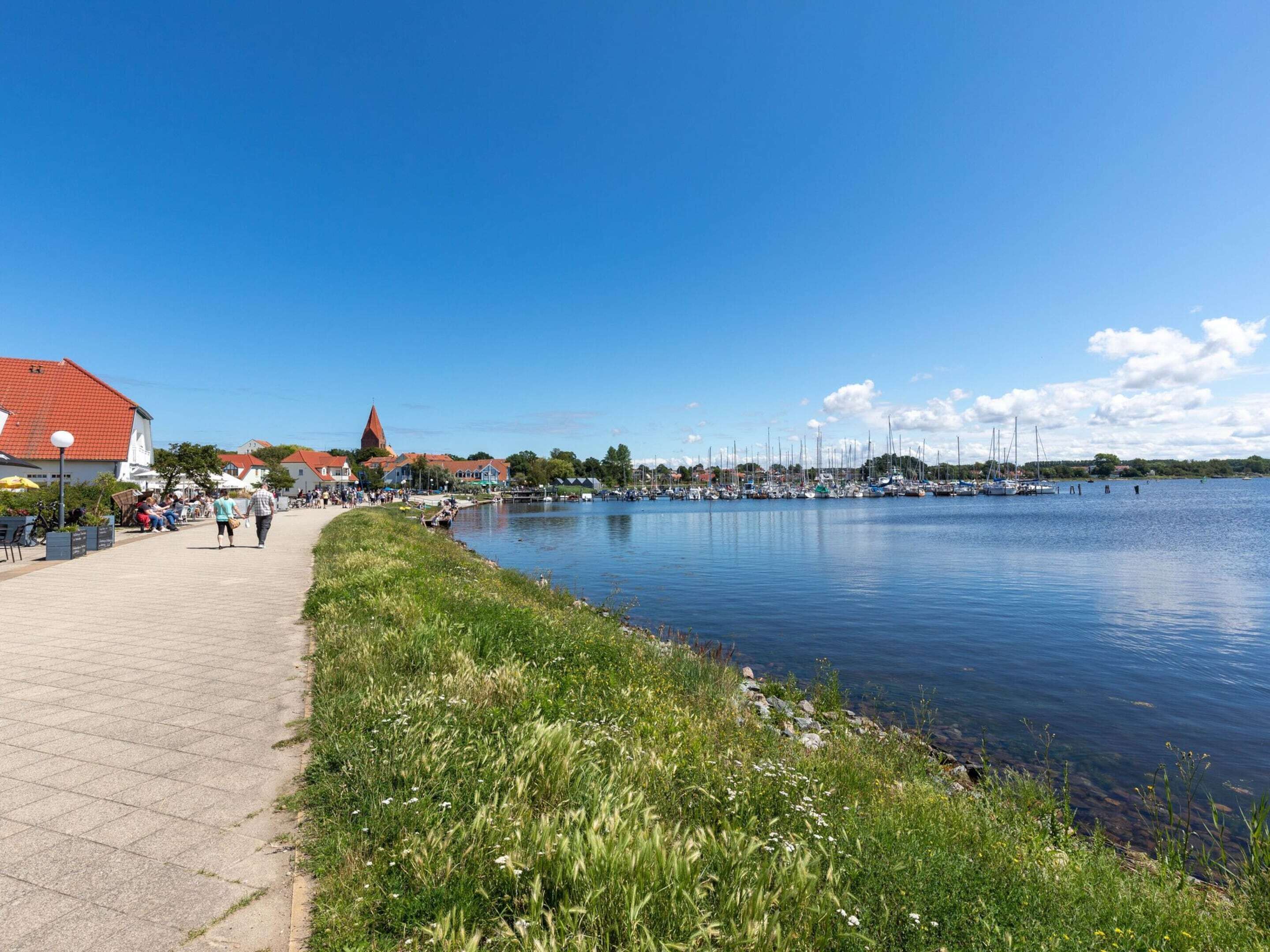 En sti langs floden med udsigt til både og bygninger.