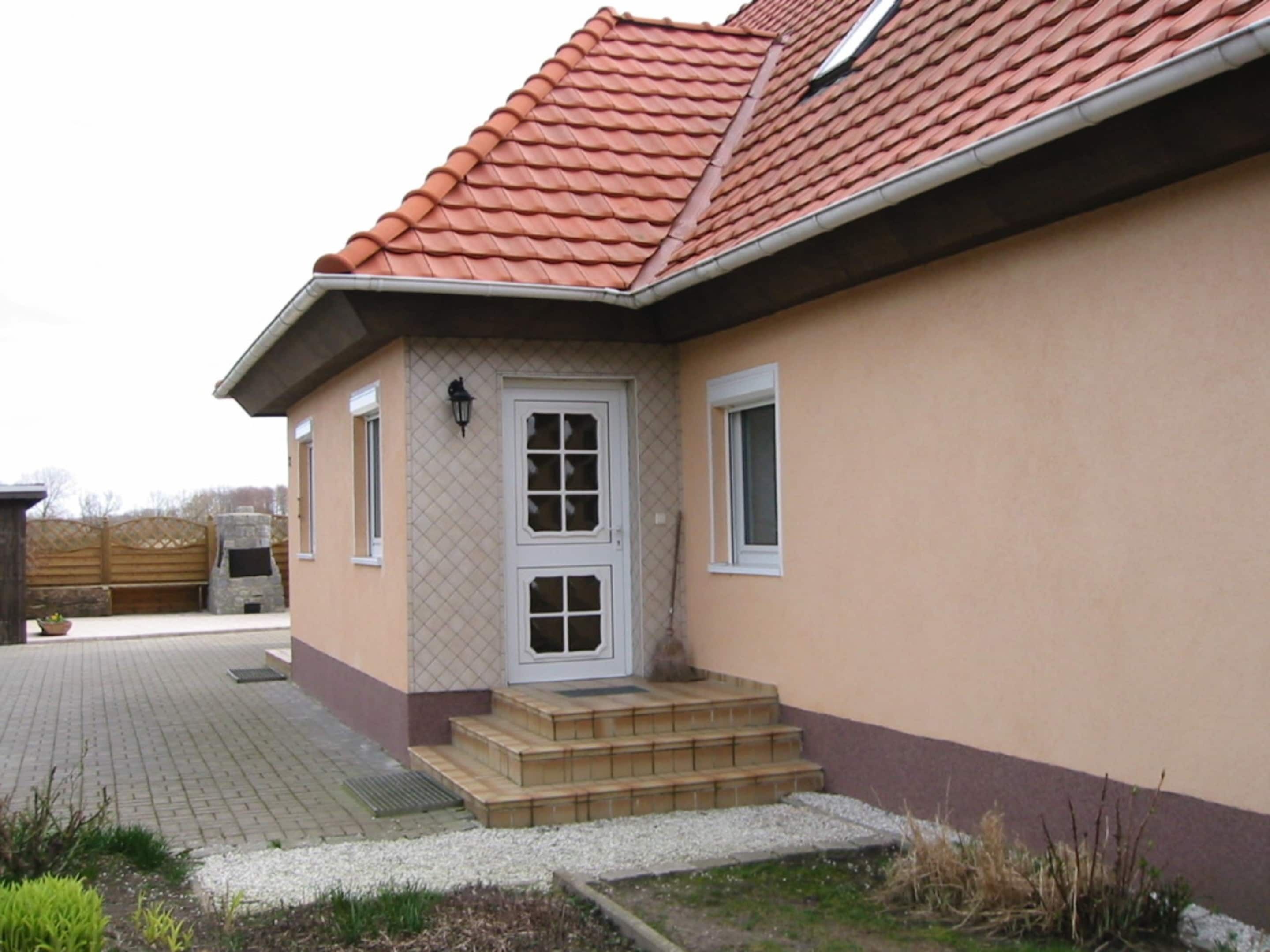 Een huis met een rode pannendak, een beige gevel en een voordeur met een klein portaaltje.