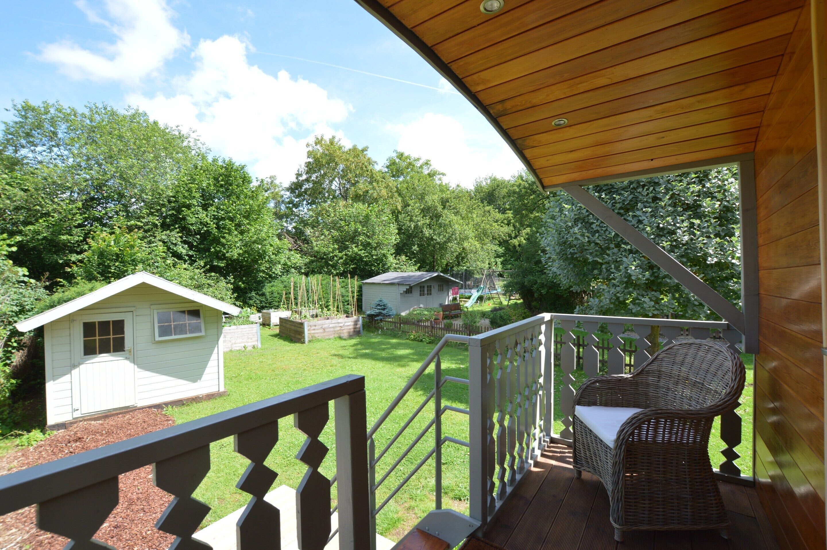 A covered porch with a wicker chair and a small shed in the background.