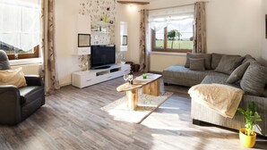 Uma sala de estar com televisão de tela plana, sofá, mesa de centro e um vaso com planta.