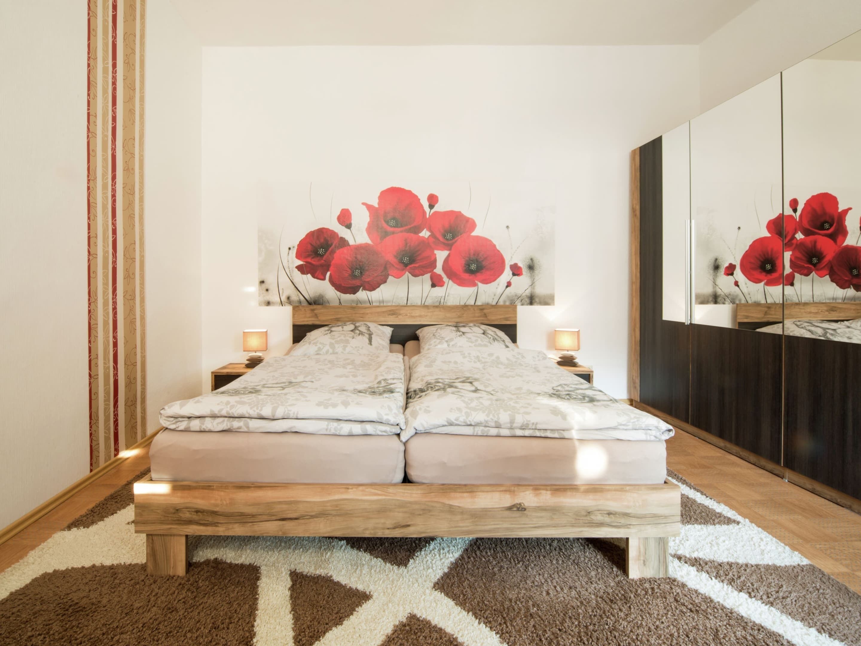 Een slaapkamer met een houten bedframe, een grote spiegel en een schilderij van een klaproos boven het bed.