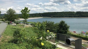A lakeside view with a grassy area, a metal fence, and a boat dock. - Seeblick-flucht in Langscheid (Sundern)