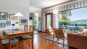 A spacious living area with a wooden dining table, wicker chairs, and a sofa. There is a balcony with a view of greenery and a table set with flowers. - Seeblick-flucht in Langscheid (Sundern)