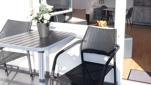 A modern outdoor dining area with a table and two chairs, a potted plant, and a kitchen in the background. - Apartment in Mullerthal With Balcony (Bollendorf)