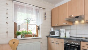 A kitchen with wooden cabinets, a microwave, a coffee maker, and a window with a view of flowers. - Cozy Ski Base With Garden (Breitenbrunn/Erzgeb.)