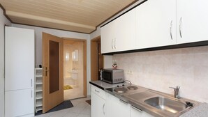 Una cocina con armarios blancos, un microondas, un lavabo y una puerta de madera que da a otra habitación.