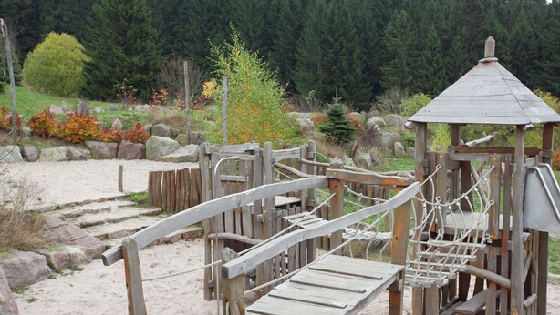 Un parque infantil de madera con un puente de cuerda, una red de escalada y un pequeño refugio.