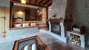 A cozy living room with a stone fireplace, wooden beams, and a stone wall. - Charming Cottage in a Farm With Views (Doische)