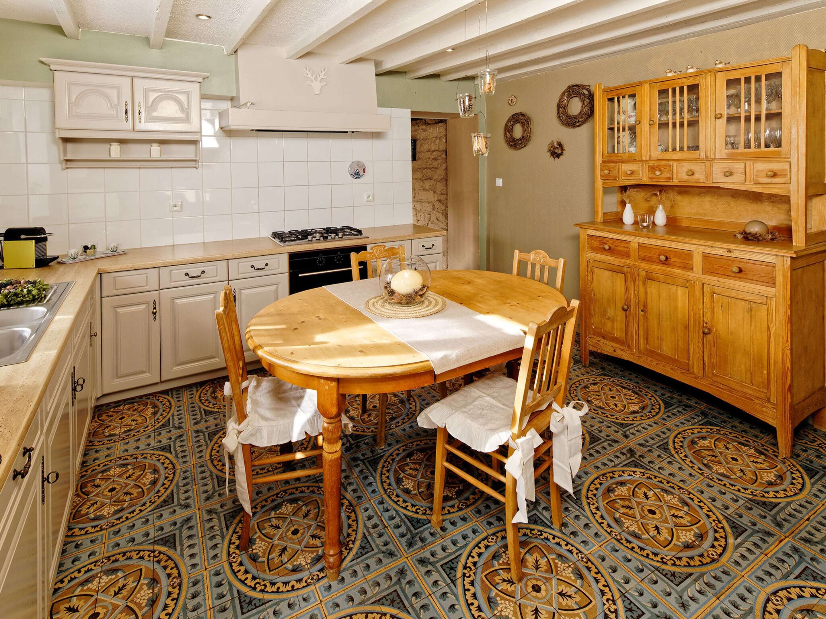 A kitchen with a round wooden table, chairs, a stove, and a wooden cabinet with glass doors.