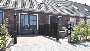 A brick building with a tiled roof, a gated entrance, and a signpost with room names. - Apartment in North Holland Near Beach (Callantsoog)