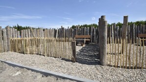 A wooden fence with a bench in the middle, gravel ground, and a clear sky. - Apartment in North Holland Near Beach (Callantsoog)