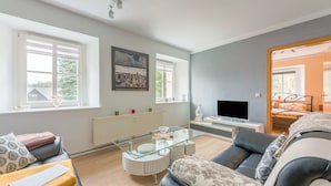 Uma sala de estar moderna com um sofá, uma mesa de centro de vidro, uma TV e uma cama ao fundo.