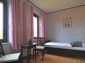 Une chambre à coucher avec un lit, une chaise, une table et une fenêtre ornée de rideaux roses.