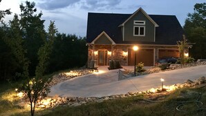 A two-story house with a stone facade, a dark roof, and a driveway leading to the garage. - SMITH TREEHOUSE LAKE LURE: CLOSE TO ASHEVILLE AND TYRON WITH KILLER VIEWS (Mill Spring)