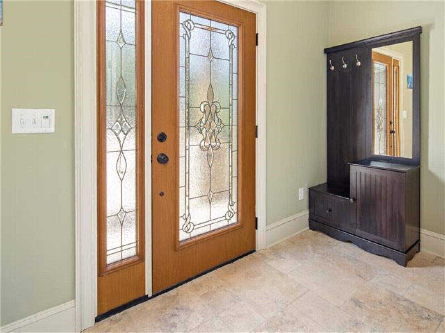 A hallway with a wooden door with glass panels, a dark wooden cabinet, and a tiled floor.