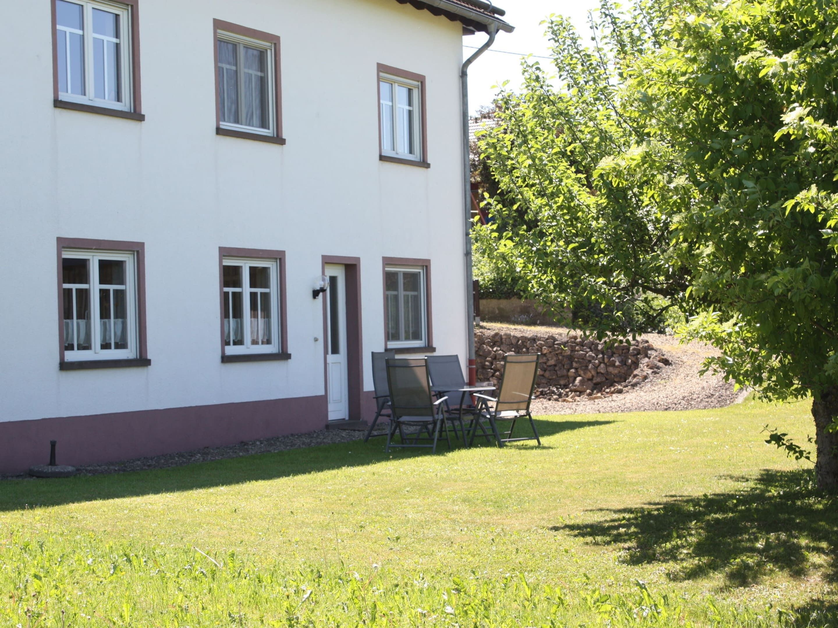 A white building with multiple windows and a door, a grassy lawn, and a tree.