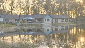 Un bâtiment situé au bord d’un lac, dont le reflet se mire dans l’eau, et qui est entouré d’arbres.