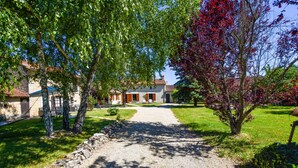 A gravel path leading to a stone building with a red-tiled roof, surrounded by trees and a stone wall.