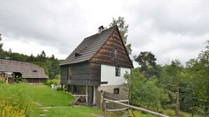 A traditional wooden house with a steeply pitched roof, surrounded by a stone wall and a wooden fence. - Holiday Home in Nejdek in West-bohemia With Garden (Nejdek)