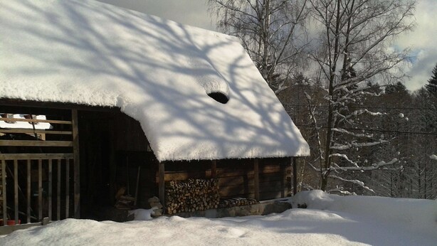 A wooden cabin with a snow-covered roof, a wooden door, and a stack of firewood outside. - Holiday Home in Nejdek in West-bohemia With Garden (Nejdek)