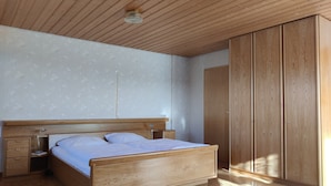 A bedroom with a wooden bed, nightstands, a wardrobe, and a ceiling light fixture.