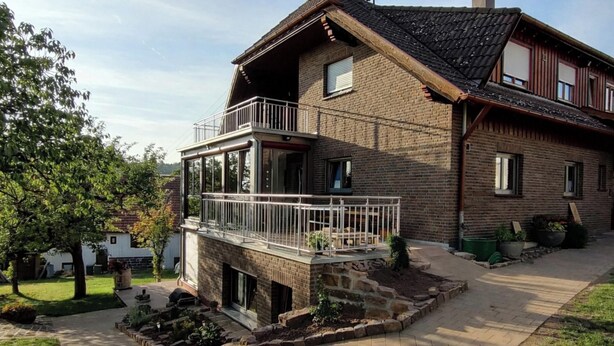 A two-story house with a balcony, a brick exterior, and a paved driveway.