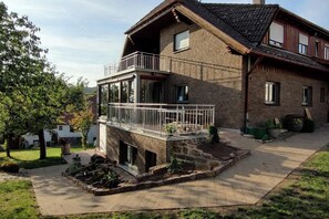 A two-story house with a balcony, a brick exterior, and a paved driveway. - Ferienwohnung Marianne in Neuweiler (Neuweiler)