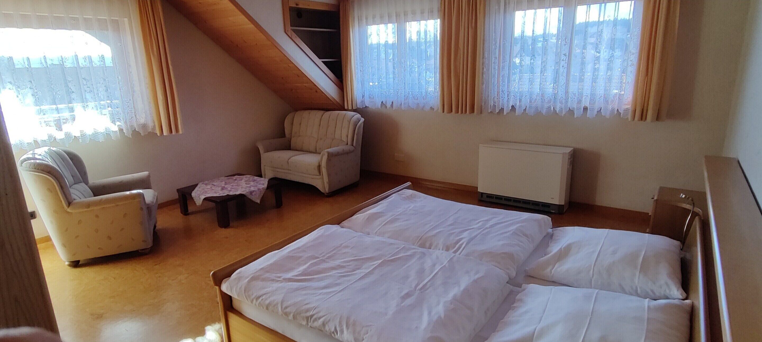 A bedroom with a bed, a chair, a small table, and a radiator.