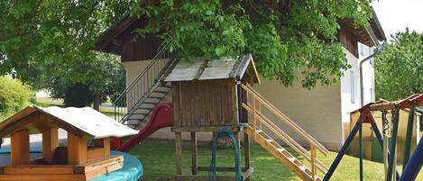 A playground with a slide, climbing steps, and a small wooden house.