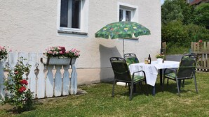 An outdoor patio with a table and chairs, a green umbrella, and a white fence with flowers. - Ferienhaus mit Garten in Waldnahe (Arnschwang)