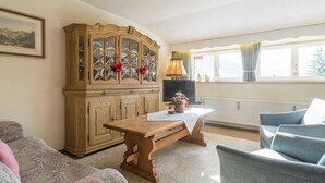 A cozy living room with a wooden cabinet, a television, a table with a vase, and a window with curtains. - Apartment in Riezlern Near Ski Slope (Mittelberg)