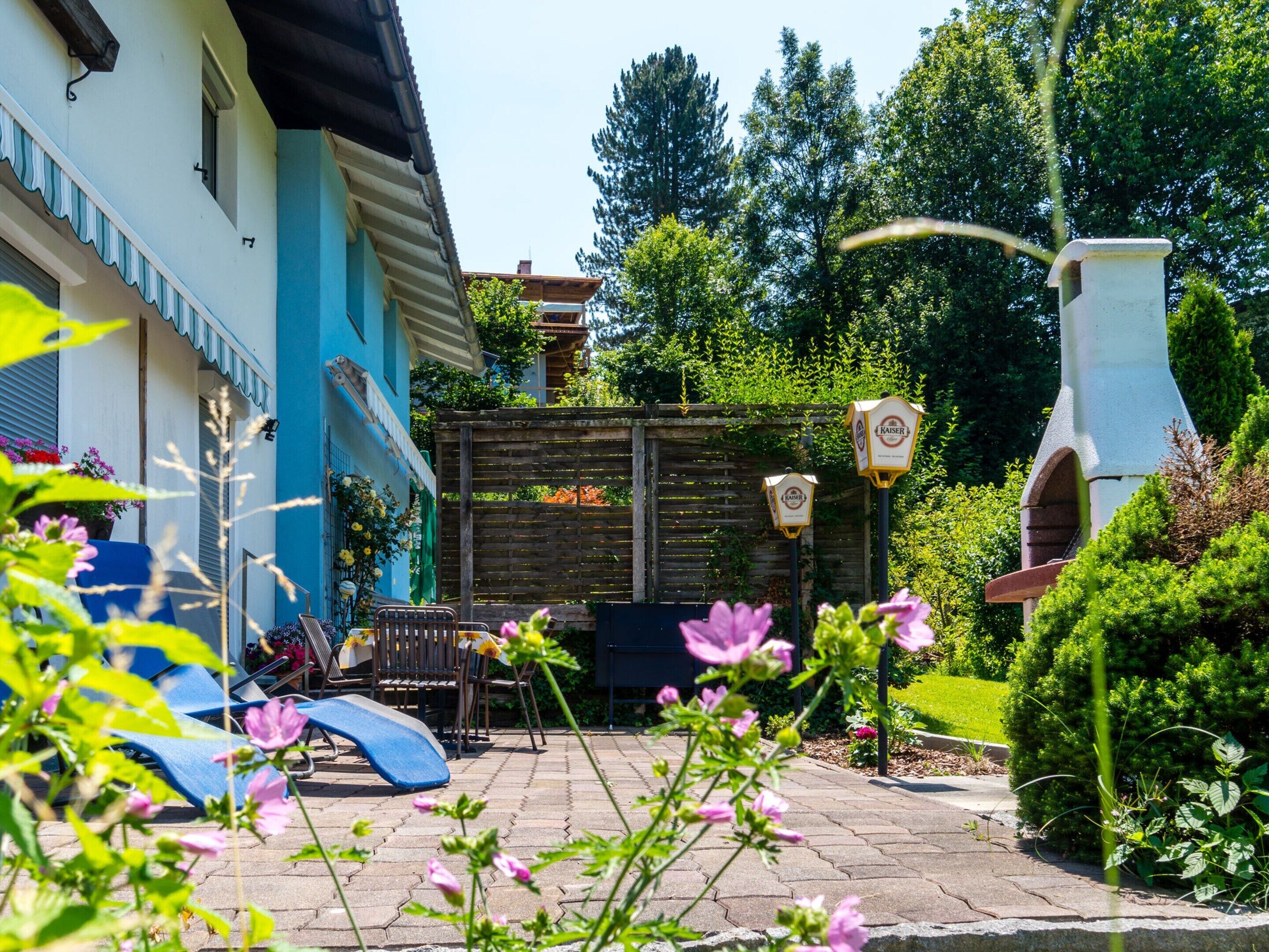 A courtyard with a blue building, a wooden fence, a barbecue grill, and a seating area with chairs and a table.