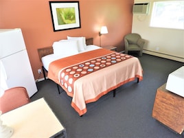 A hotel room with a bed, a chair, a desk, and a refrigerator.