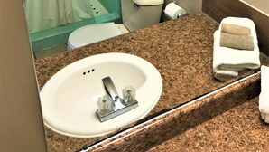 A bathroom with a white sink, a toilet, a shower with a green tiled wall, and a towel on the counter. - Country Meadow inn (South Lyon)