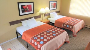A hotel room with two beds, a nightstand, a lamp, and two framed pictures on the wall. - Country Meadow inn (South Lyon)