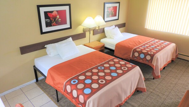 A hotel room with two beds, a nightstand, a lamp, and two framed pictures on the wall. - Country Meadow inn (South Lyon)