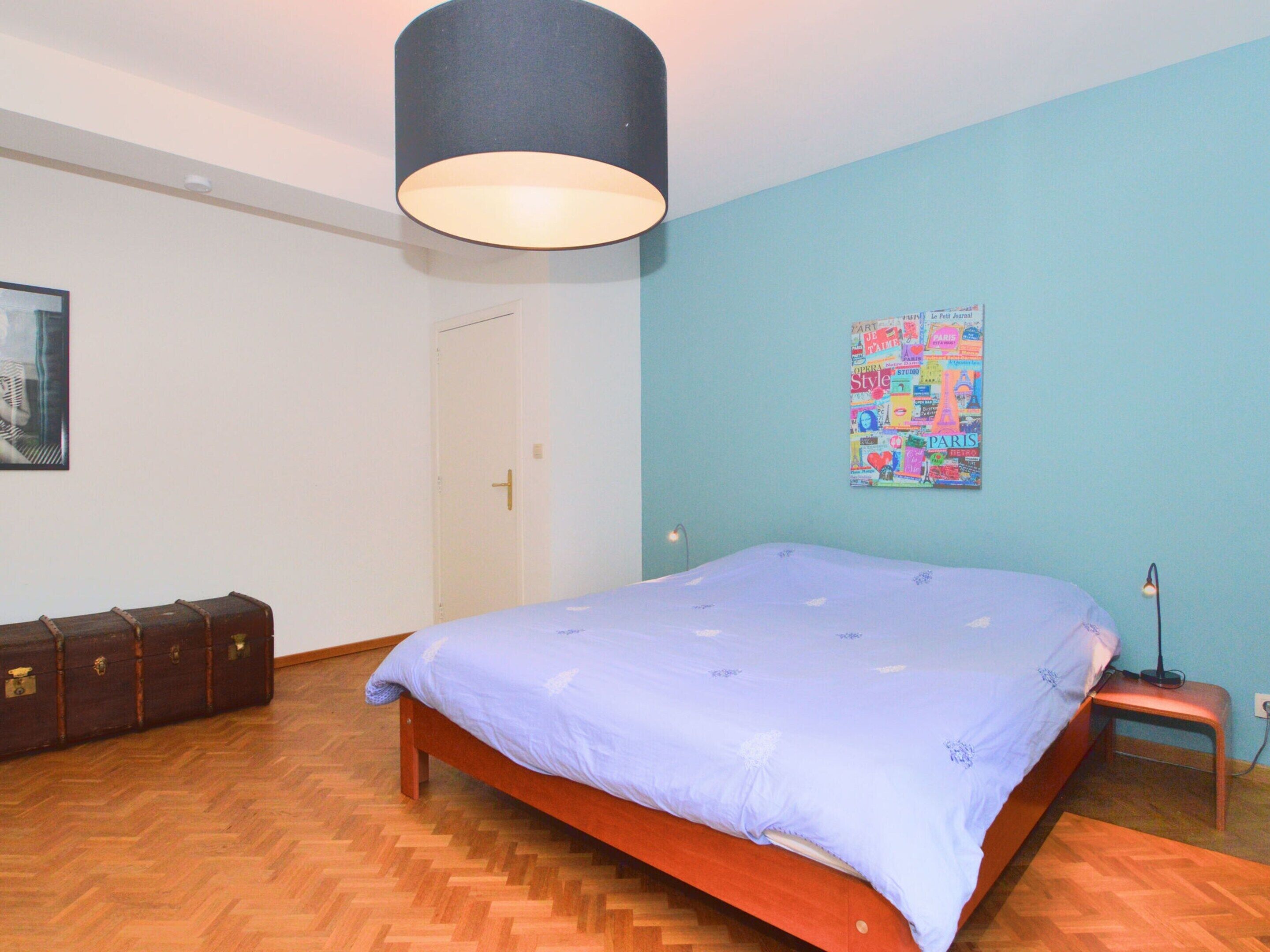 Una camera da letto con un letto di legno, una parete blu, un poster, una valigia e una porta.
