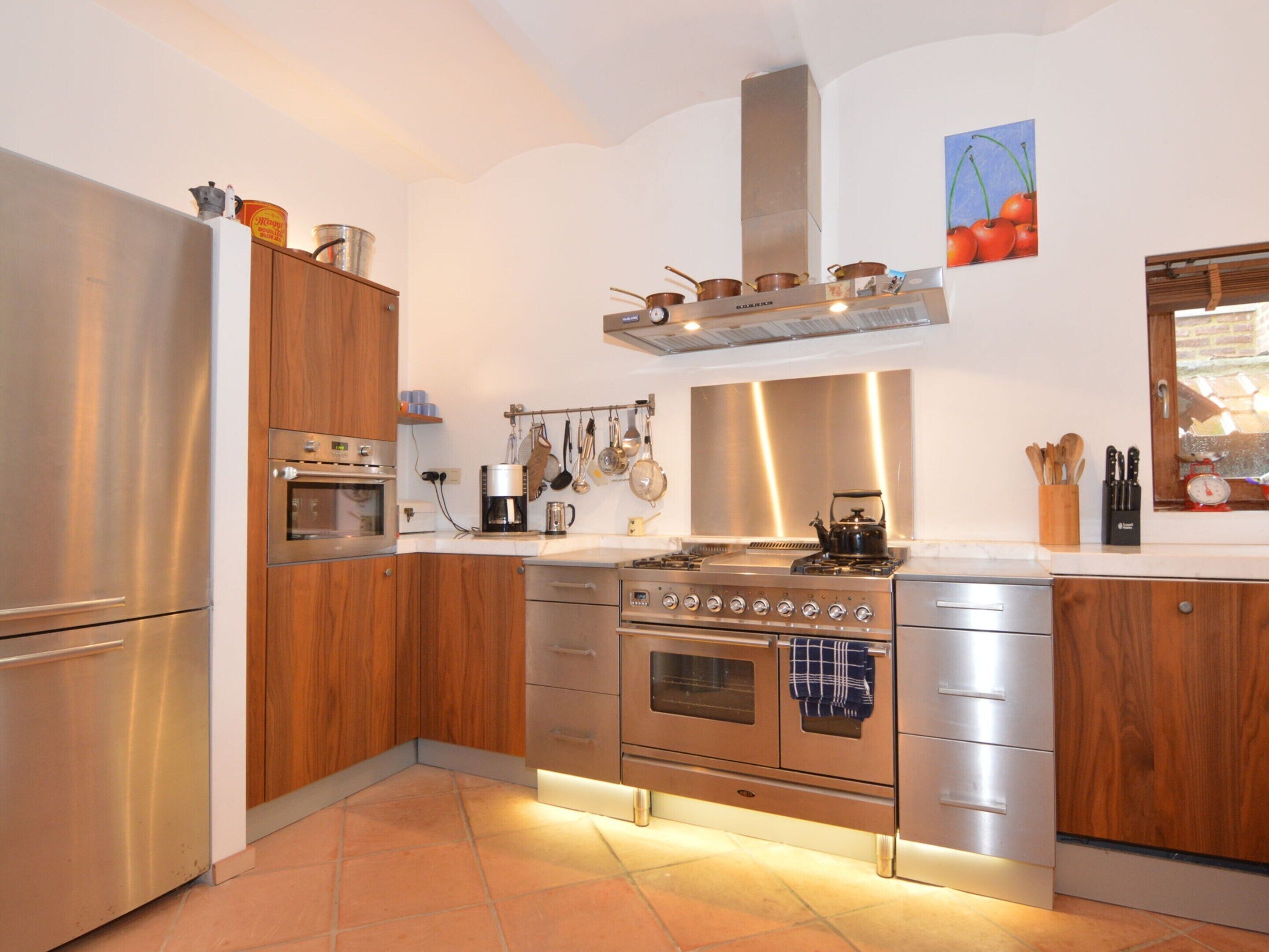 Une cuisine moderne dotée d’appareils électroménagers en acier inoxydable, de meubles en bois et d’un sol carrelé.